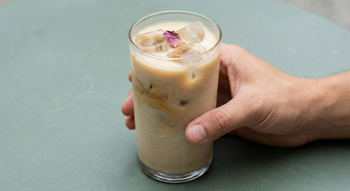 Verre d'AGHRUM au lait parsemé de pétales, tenu à la main